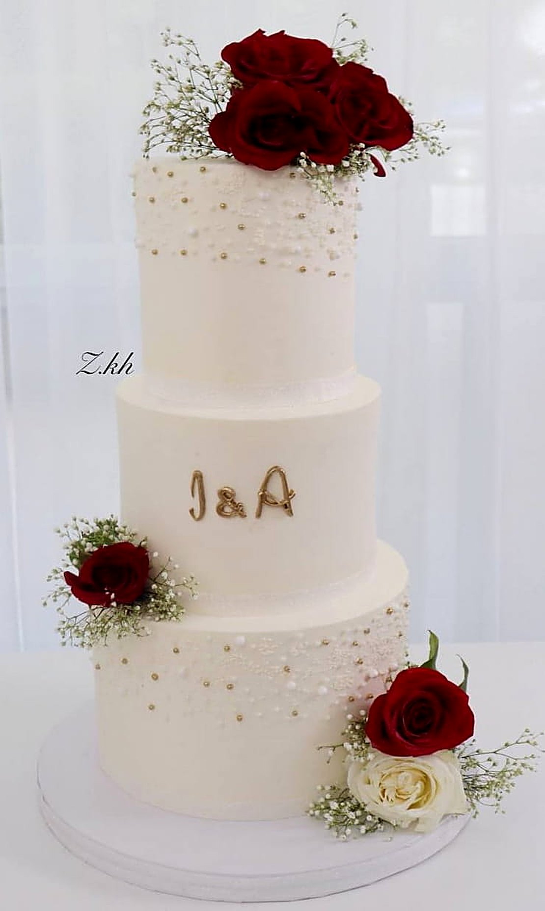 Three-tier pearl-dotted wedding cake with red roses and the initials I & A