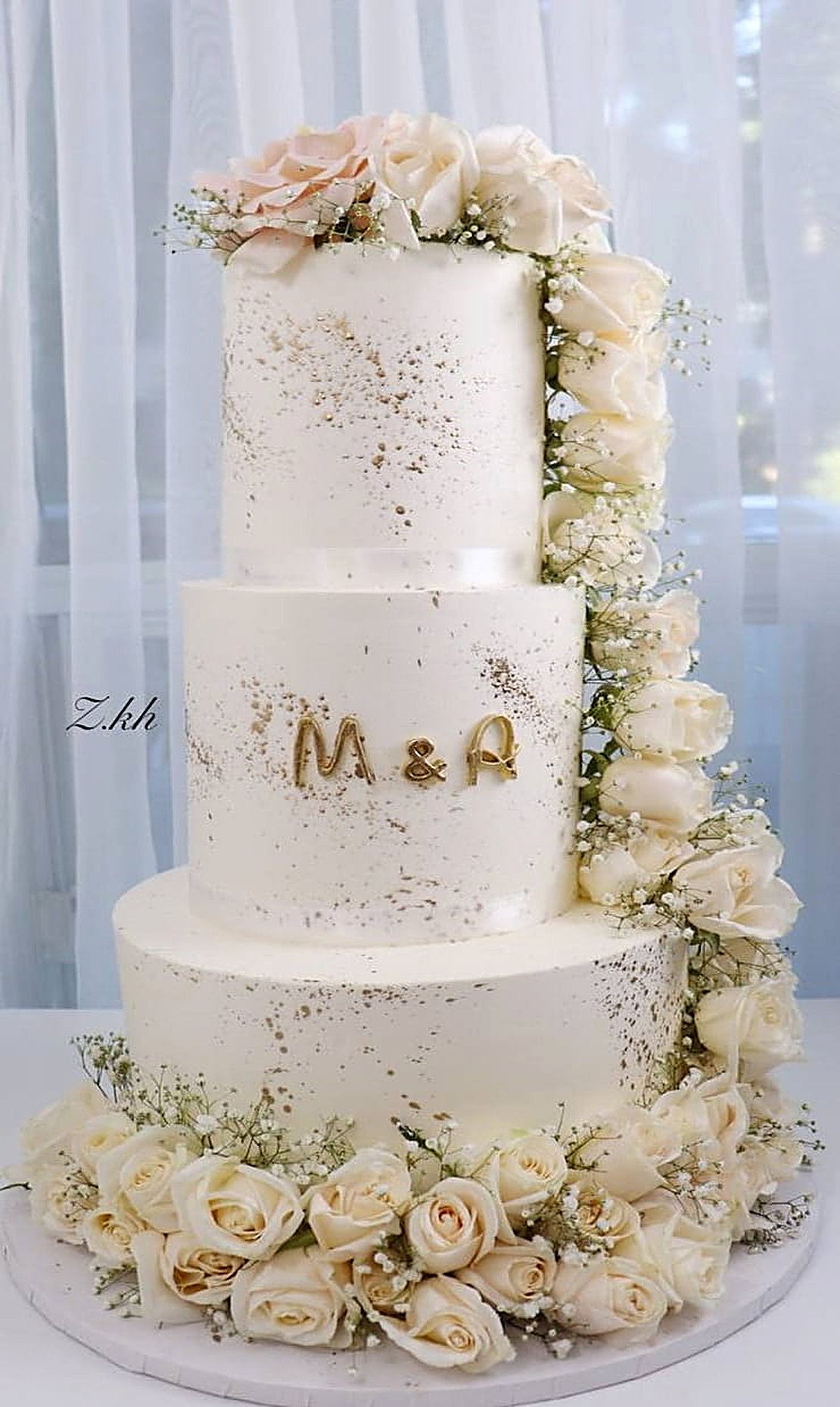 Three-tier wedding cake with gold flecks, cream roses and the initials M & A