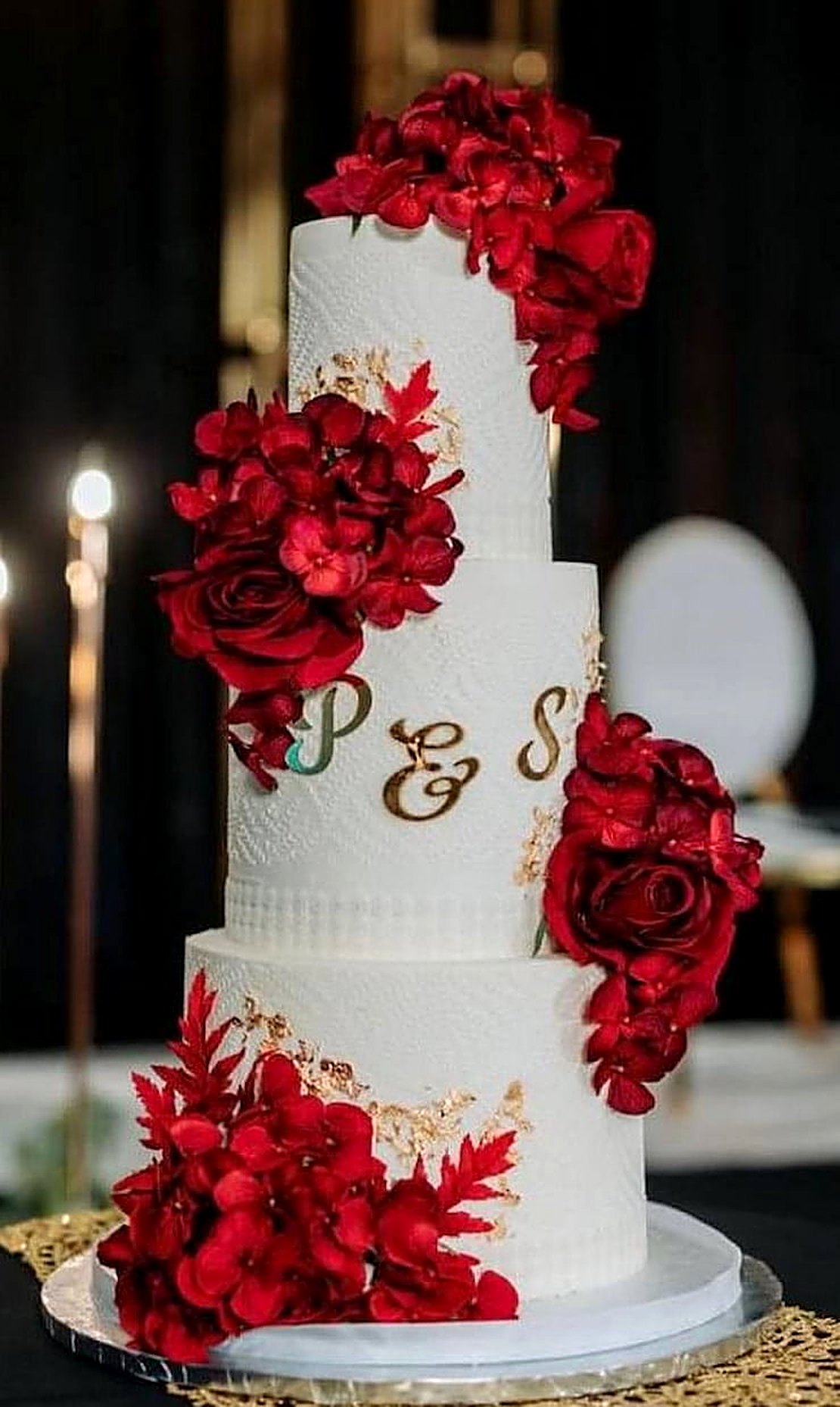 Three-tier white wedding cake with red sugar roses and the initials P & S